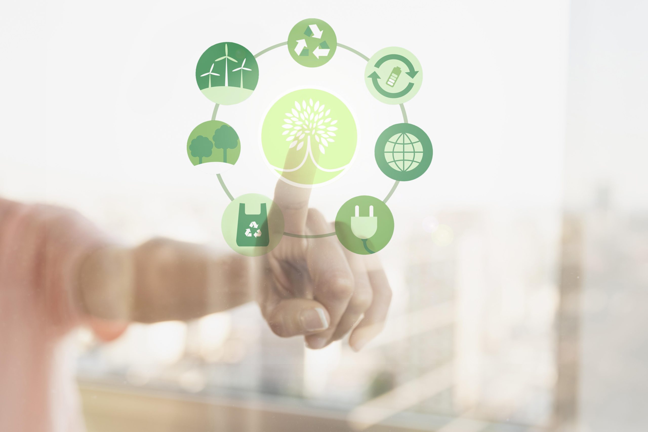 Pessoa tocando em uma tela transparente com ícones verdes relacionados à sustentabilidade, incluindo energia renovável, reciclagem, reutilização, preservação de árvores, sacola reciclável, conexão global e energia limpa, em torno de um símbolo central de árvore estilizada