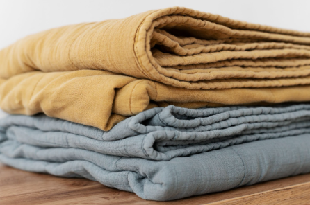 Cobertores reciclados dobrados sobre superfície de madeira, simbolizando reaproveitamento têxtil e sustentabilidade ambiental.