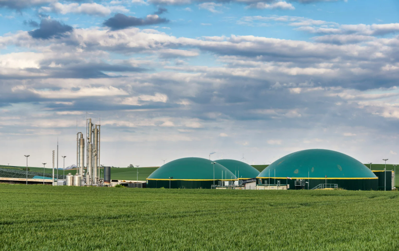 Usina de geração de biometano com biodigestores de cúpula verde em meio a uma área rural, ilustrando a infraestrutura necessária para a produção de energia limpa e renovável.