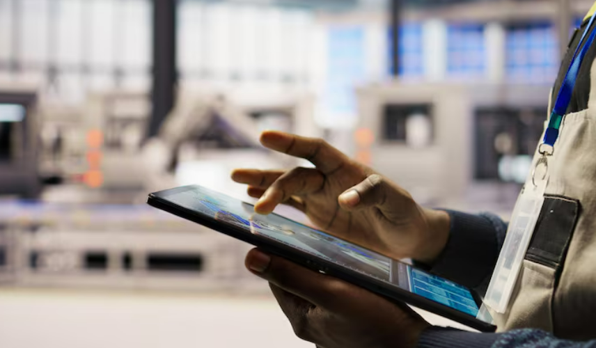 Close das mãos de um profissional utilizando um tablet para monitorar dados em um ambiente industrial. A imagem representa o uso de tecnologia para preparar a indústria para fiscalizações ambientais, garantindo a conformidade e evitando multas.