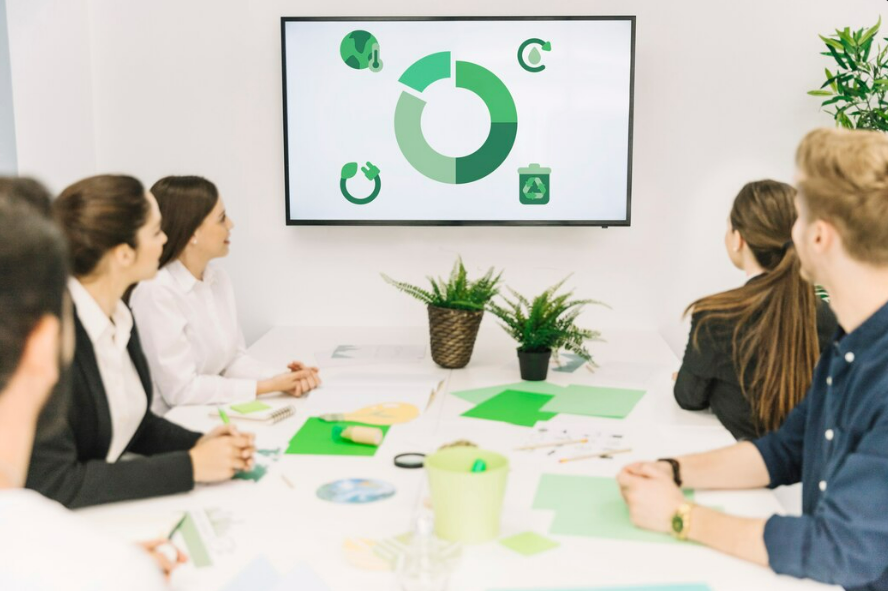 Equipe de profissionais em uma sala de reunião assistindo a uma apresentação em uma tela com gráficos e ícones de sustentabilidade. Imagem representando o planejamento de uma operação in company para melhorar o controle e a rastreabilidade na gestão de resíduos.